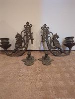 Pair of antique metal wall mount candle holders with matching dragon design and separate mounting plates. Shown on carpeted floor for scale.