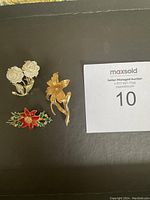 Three brooches displayed on black background showing floral and festive designs.