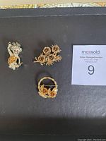 Three assorted brooches: cat with rhinestones, gold-tone rose cluster, gold-tone basket with roses
