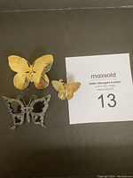 Four butterfly brooches including one large gold-tone and one smaller gold butterfly, plus two silver-tone rhinestone butterflies with auction card.