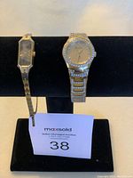 Two metal bracelet watches displayed on black stand with auction lot number 38 card, showing Bulova watch on right with extended strap, and rectangular-faced watch with gold-tone bracelet on left.