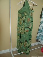 Green tropical print pantsuit hanging on white plastic hanger on rack