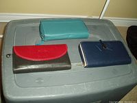 Three wallets: teal zipper wallet, dark olive wallet with red flap, navy blue wallet with zipper