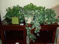 Five assorted faux greenery arrangements featuring ivy and fern plants displayed on wooden tables