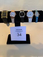 Front view of five assorted watches displayed on a black watch holder stand.