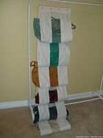 Six assorted ladies purses organized vertically on a white fabric and metal hanger holder, showing various colors