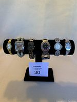 Six metal bracelet watches displayed on black watch holder with label "30" in front
