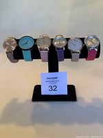 Photo showing 6 assorted banded watches displayed on a black stand with a MaxSold auction card in front