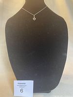 Photo of silver-tone necklace with small open heart pendant displayed on black bust