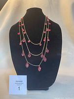 Layered silver-tone chain necklace with multiple pink teardrop-shaped beads displayed on a black bust stand.