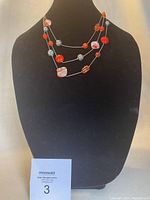 Multi-strand necklace with red and silver beads displayed on black bust