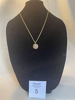 Gold-tone chain necklace with flower pendant featuring clear stones displayed on black bust.