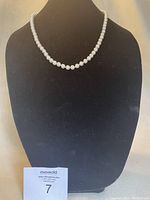 White pearl-style bead necklace displayed on black stand