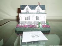 Front view of the miniature house sculpture showing the porch, windows, chimney, and garden base with figurines.