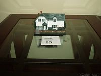 Front view of the Green Gables House model on glass table showing details of the white house with green roof, windows, and river rock ground effect base.