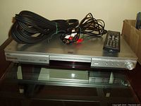 Silver Samsung DVD player with remote and various AV cables placed on glass surface.