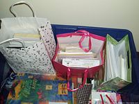 Three bags containing assorted greeting cards, envelopes, and gift bags on a blue plastic container.