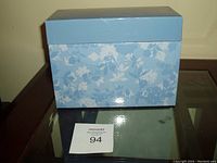 Blue floral patterned cardboard box closed, placed on glass table.