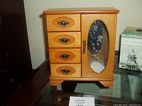 Front view of the wooden jewelry box with four drawers and a glass door showcasing floral etching and brass handles.