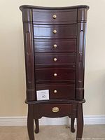 Front view of closed wooden jewelry cabinet showing six drawers and gold-tone knobs
