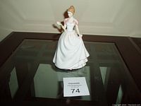 Front view of porcelain figurine of woman in white and pink gown holding pink flower