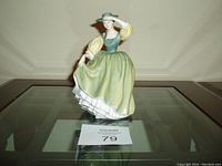 Front view of the Buttercup porcelain figurine on a glass table with the item card showing number 79.
