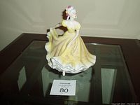 Front angle view of Royal Doulton Ninette figurine in yellow dress on glass top table