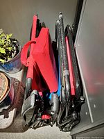 Folded view of three zero gravity chairs showing two red adult-sized and one blue kids-sized chair folded and stacked vertically with visible neck cushions and black metal frames.