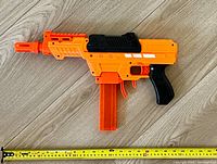 Orange and black Adventure Force Nexus NERF blaster laid flat against a wood surface with a measuring tape showing length of approximately 18 inches.