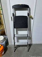 Full view of the aluminium step ladder showing two steps and top tray, ladder folded and standing upright against a wall.