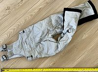 Light gray ski pants showing front side with elastic suspenders, snap buttons at cuffs, zippered and buttoned pockets.