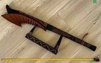 Photo of a large carved wooden Fijian neckbreaker weapon with a decorative stand on a wood floor, measuring tape showing length near 40 inches.