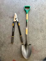 Photo showing Fiskars shears with ergonomic black and yellow handles next to a high-quality shovel with wooden handle and green plastic D-grip.