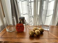 Group photo of all glass vases and decor items on a wooden table in front of a window with sheer curtains.