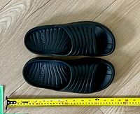 Top view of black Hoka One One recovery slides showing contoured footbed and size comparison with measuring tape.