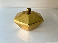 Hexagonal brass container with hammered texture and a round knob handle on the lid, viewed from an angle.