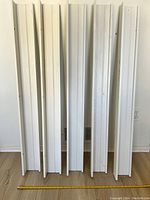 Five white IKEA Mosslanda floating shelves standing vertically against a wall with a measuring tape laid on the floor showing scale approx. 46 inches.