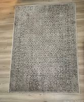 Top view photo of a rectangular grey IKEA VEDBAK rug with an ornate faded pattern on a light wooden floor.