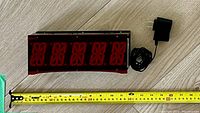 Front view of custom LED alarm clock showing large red digits with power adapter and measuring tape showing 11 inches width.