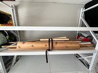 Long pine boards strapped on a shelf, some shorter pieces and dowels visible