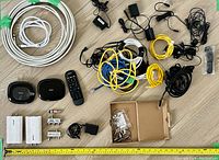 Top-down view of all lot items arranged on floor, including remotes, networking devices, cables, adapters, and connectors.