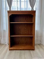 Front view of the oak veneer bookcase showing two shelves and decorative trim details.