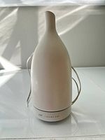 Front view of the Saje Aromatherapy Diffuser showing smooth rounded ceramic body and narrow spout with attached power cord.