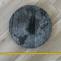 Top view of solid marble Lazy Susan showing oil stain and natural marble pattern, placed on light wooden floor with measuring tape showing approximately 24 inch diameter.