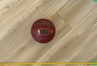 Top-down photo of a new Spalding basketball on a wooden floor with measuring tape showing size context