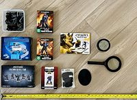 Photo showing boxed Warhammer 40K miniature sets including Space Marines Primaris Intercessors, Primaris Reivers, Deathwatch Kill Team, and a Primaris Lieutenant figure. Several loose black plastic bases and additional miniature parts in a clear container. Also included are a Citadel Palette Pad, two handheld magnifiers, and a painting handle grip.