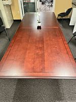 Top view of the solid wood conference table showing polished wood surface with a central cable port and subtle bordered design.