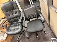 Photo showing two rolling office chairs side-by-side, one black leather and one black mesh back.