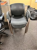 Photo of a stack of six black commercial grade stackable chairs with metal frames and plastic seats and backs, showing the chairs stacked in a neat pile.