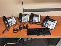 Four AT&T Model 1070 multi-line desk phones arranged in a row, along with two wired headsets and one wired keyboard in front of them, all placed on a light wood office desk.